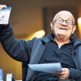 Mossèn Ramon somrient amb el llibre a la mà.