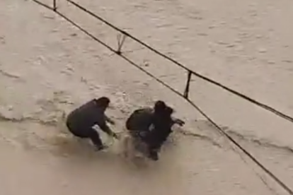 Una mare intenta travessar una riada amb el seu fill amb cotxet