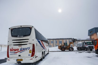 Un autocar en un aparcament del Pas mentre una excavadora treu neu de la zona.