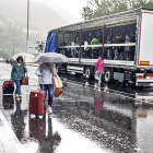 Turistes amb maletes creuant el tall de l’N-145 i manifestants resguardant-se de la pluja dins d’un camió.
