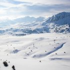 Imatge aèria de pistes d'esquí i muntanyes de fons cobertes de neu.