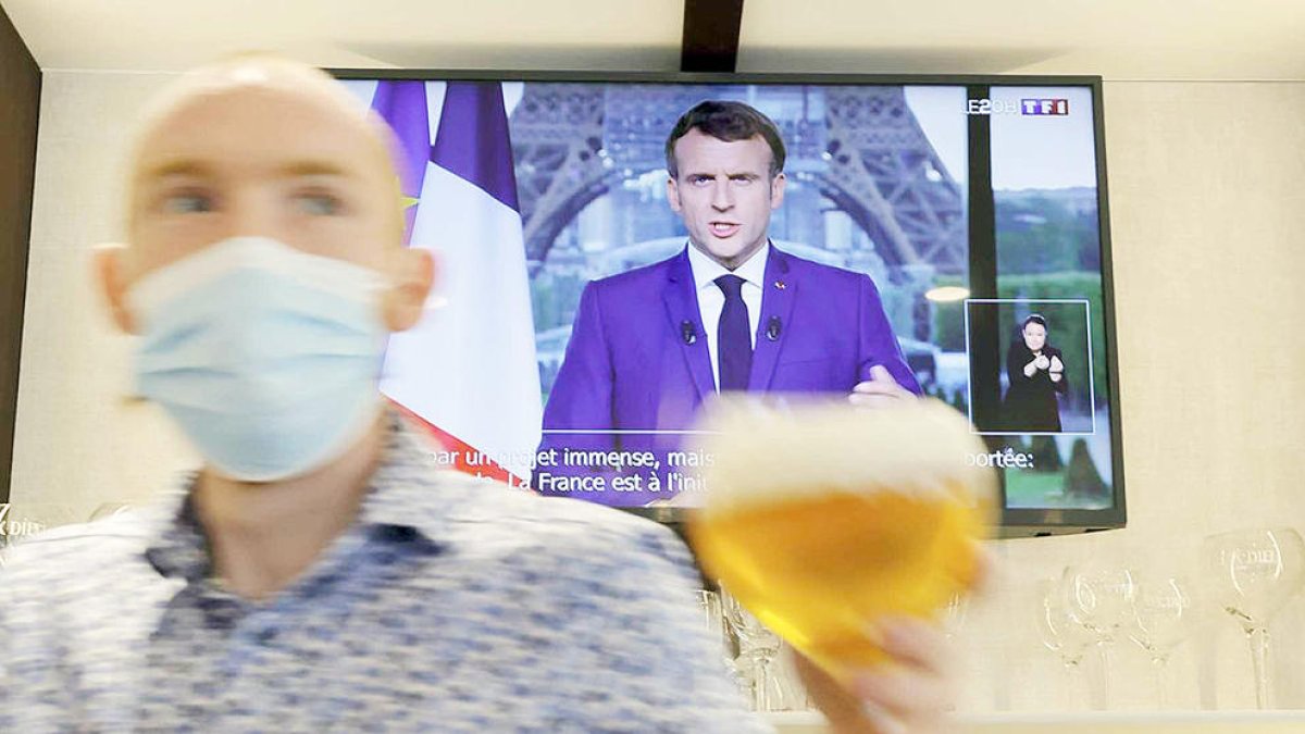 Un cambrer portant una cervesa en un bar de França amb Macron per la televisió.