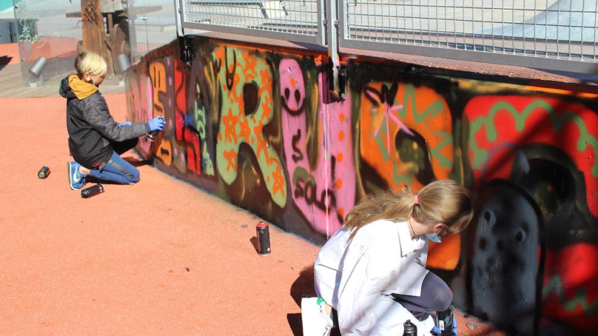 Dos nens pintant un tros de mural.