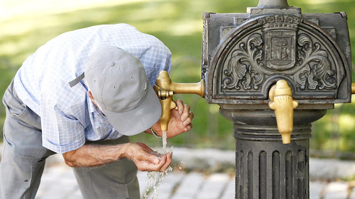 Un home bevent aigua d'una font en plena onada de calor.