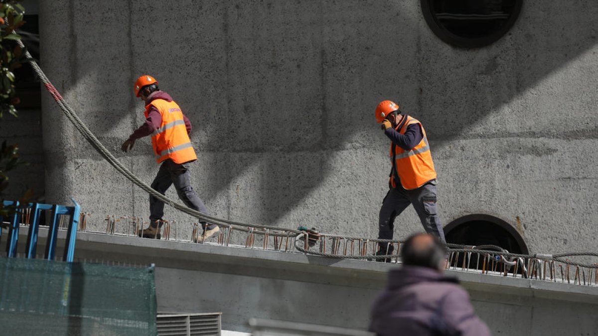 Un jubilat mira com treballen dos operaris de la construcció.