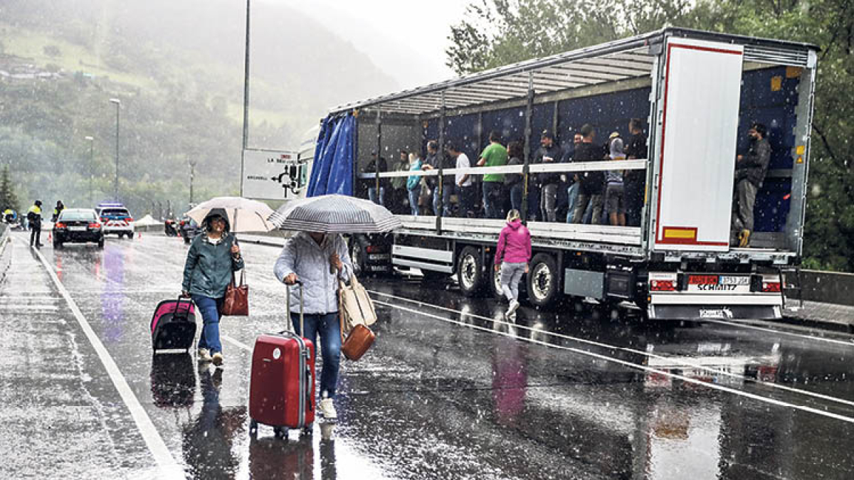Turistes amb maletes creuant el tall de l’N-145 i manifestants resguardant-se de la pluja dins d’un camió.