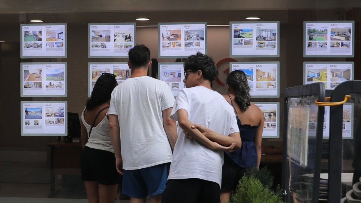 Un grup de joves mirant ofertes d’habitatges a l’aparador d’una immobiliària.