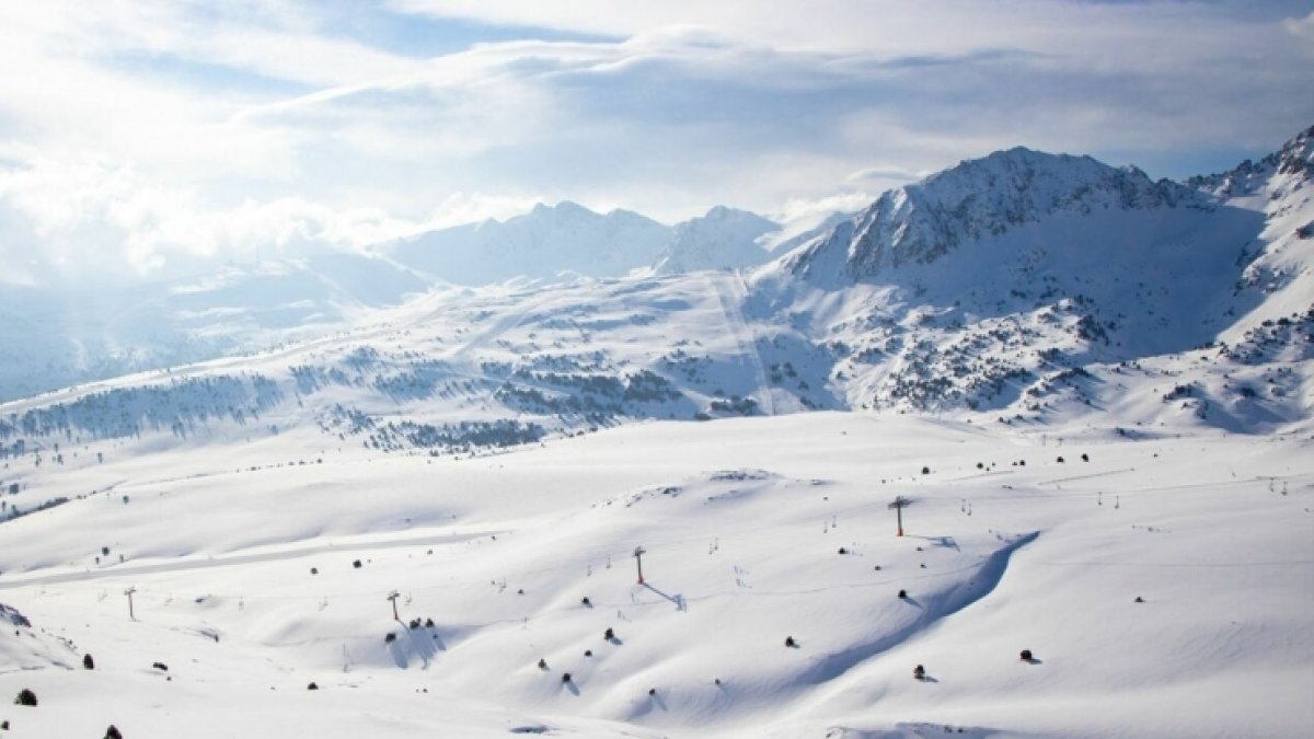 Imatge aèria de pistes d'esquí i muntanyes de fons cobertes de neu.
