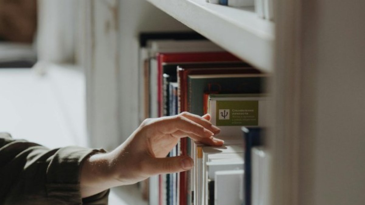 Un estudiant seleccionant un llibre en una biblioteca.
