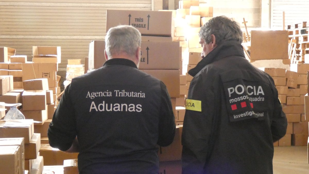 Un agent dels mossos d'esquadra i un altre de duanes de Catalunya, amb la mercaderia interceptada.